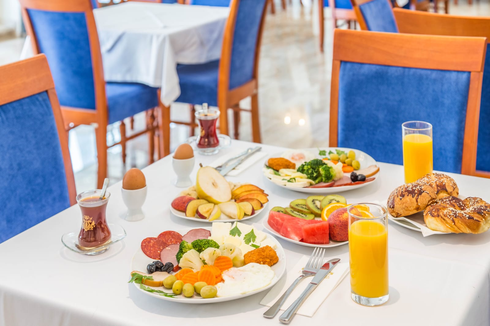 A breakfast table with fruit, pastries, eggs and orange juice