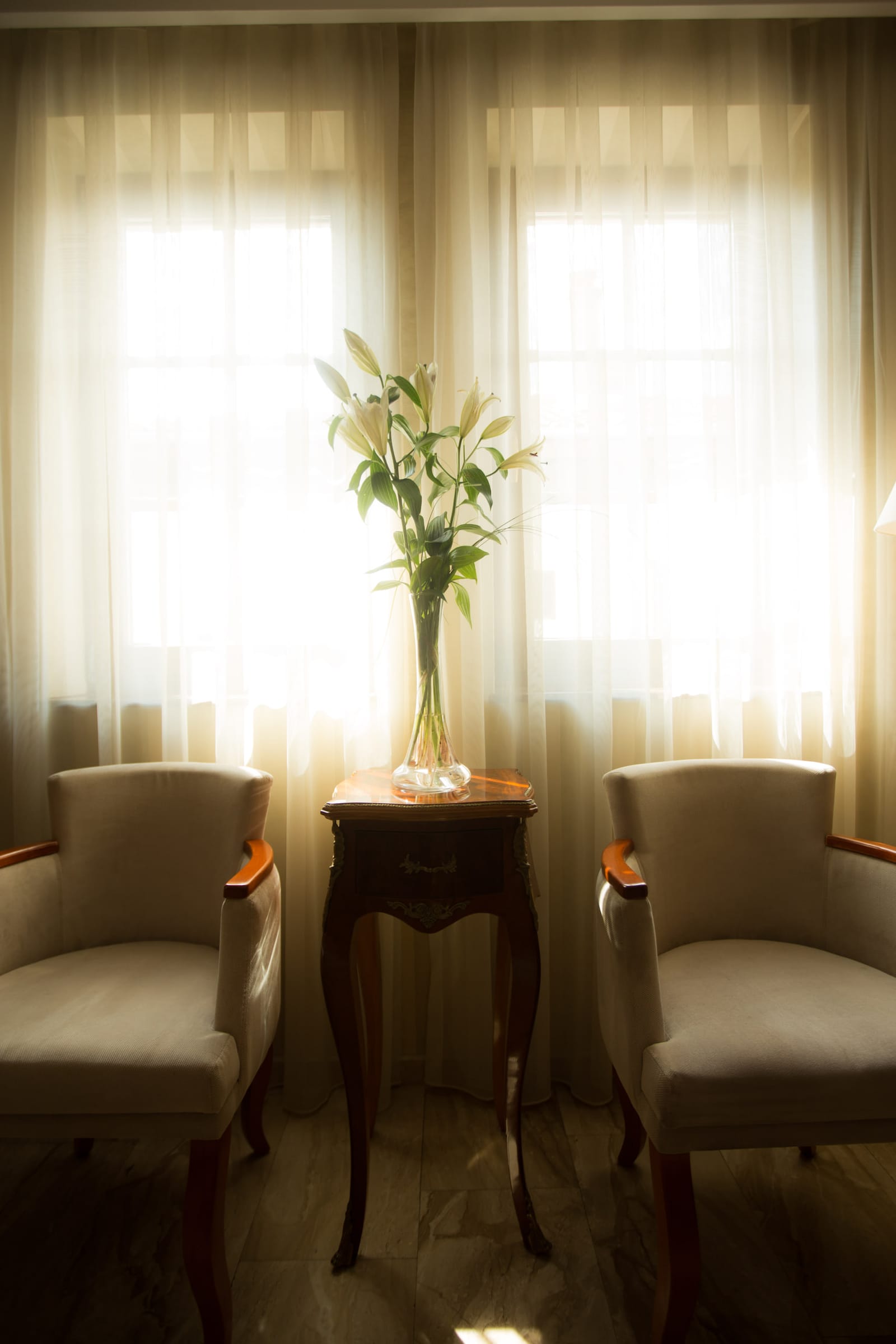 Two armchairs and a vase of white lilies in soft window light