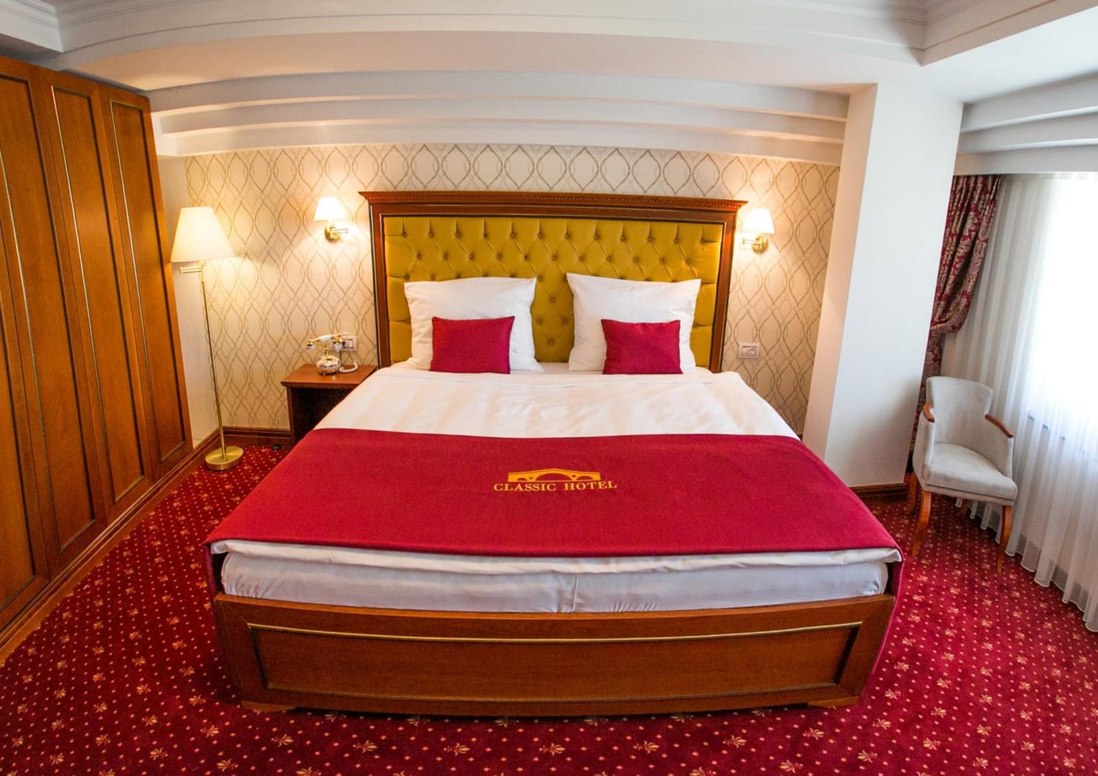Deluxe Double room with a gold tufted headboard and a crimson throw