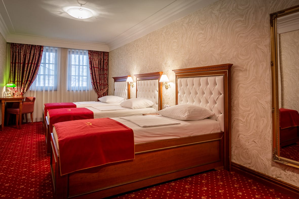 Deluxe Triple room with three single beds and a tall gilt mirror