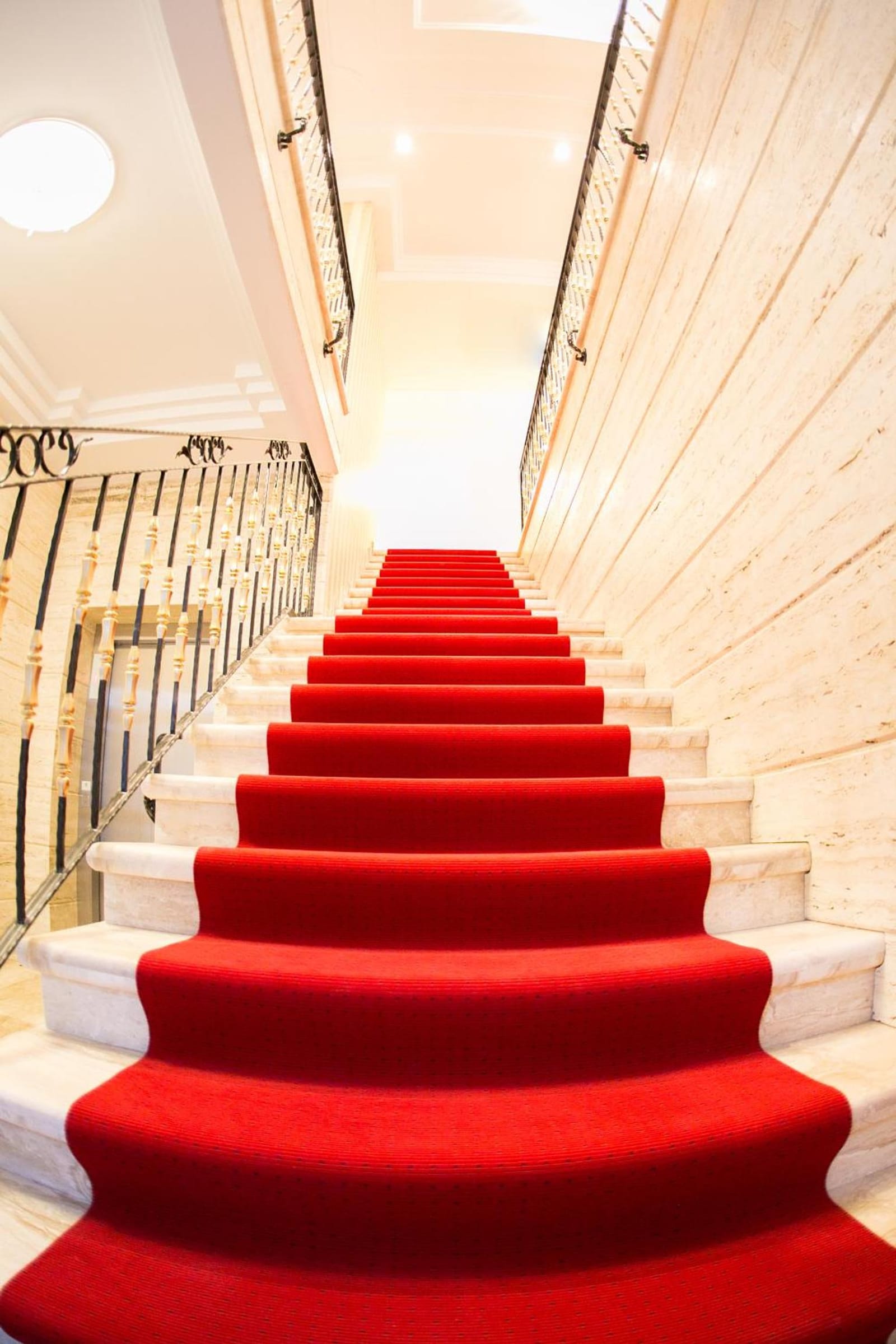 A red-carpeted marble staircase with a wrought-iron rail