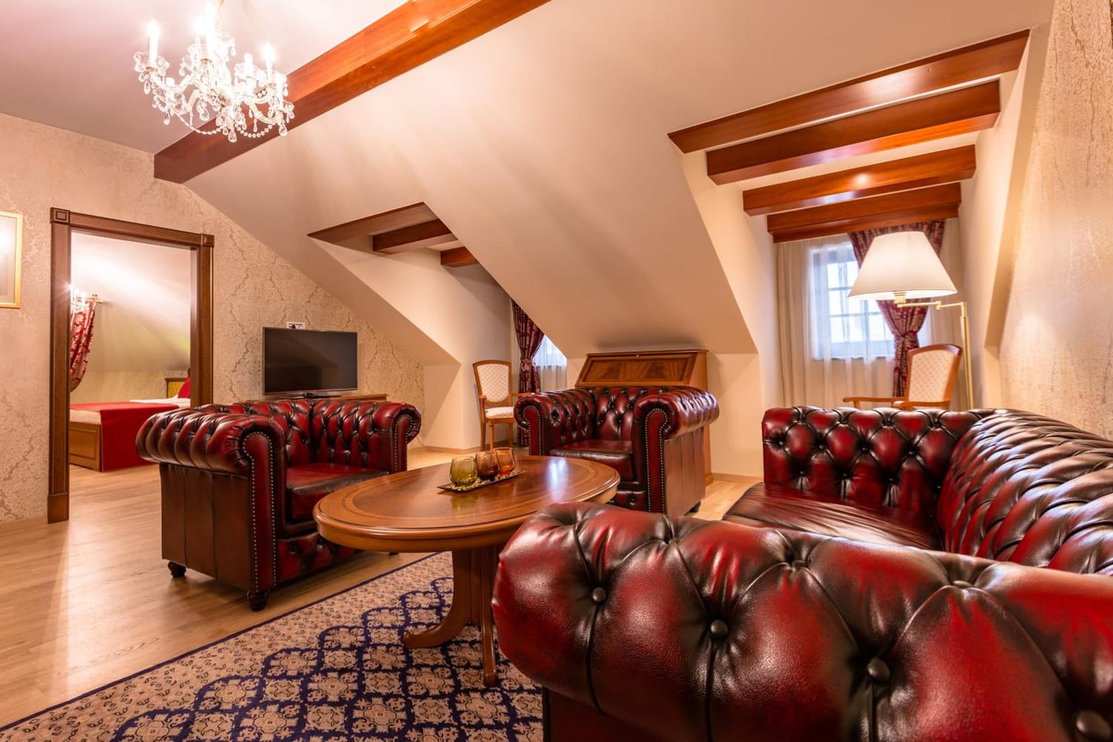 Attic suite living room with oxblood Chesterfields, crystal chandelier and timber beams