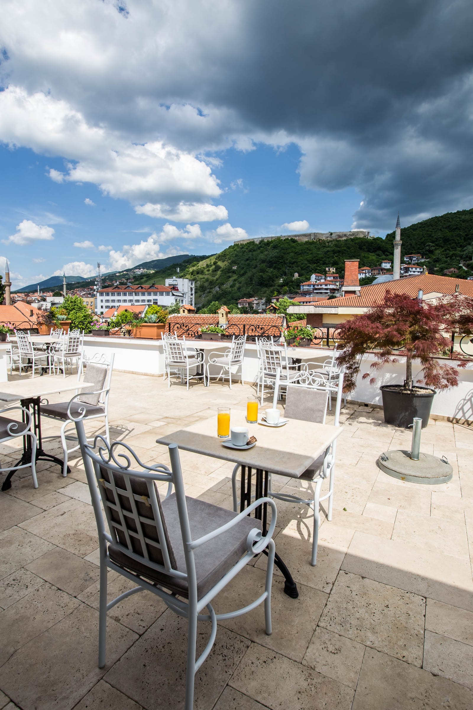 Rooftop terrace seating with blue sky and the hills of Prizren